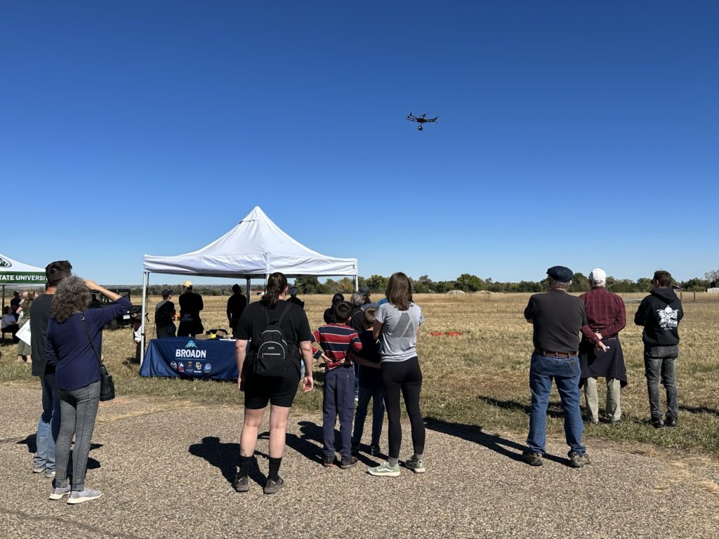 Community and industry members watch as BROADN Graduate Student Ashley E Miller pilots a drone at CSU's Drone Airshow, 2023.